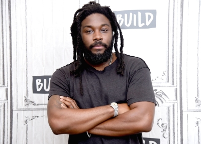 Image of Jason Reynolds in a black tshirt standing with his arms crossed, looking into the camera.