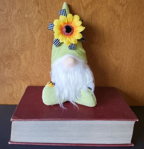 Photo of a gnome with a sunflower on his hat sitting on a large old book